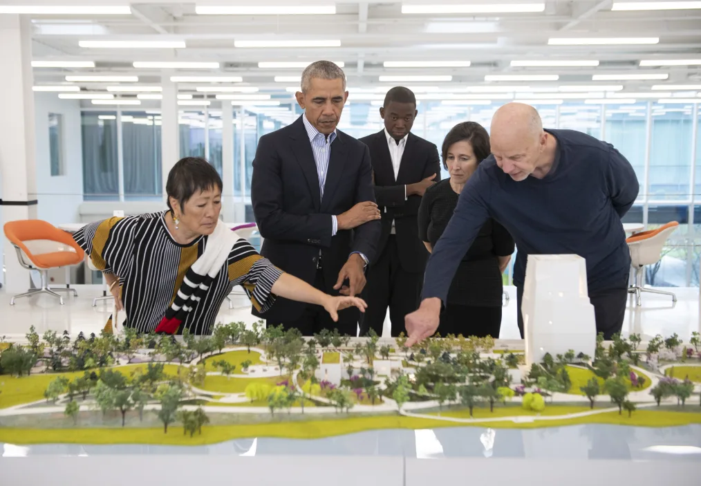 Tod Williams and Billie Tsien point to the model of the Obama Presidential Center as President Obama looks on with his arms crossed.