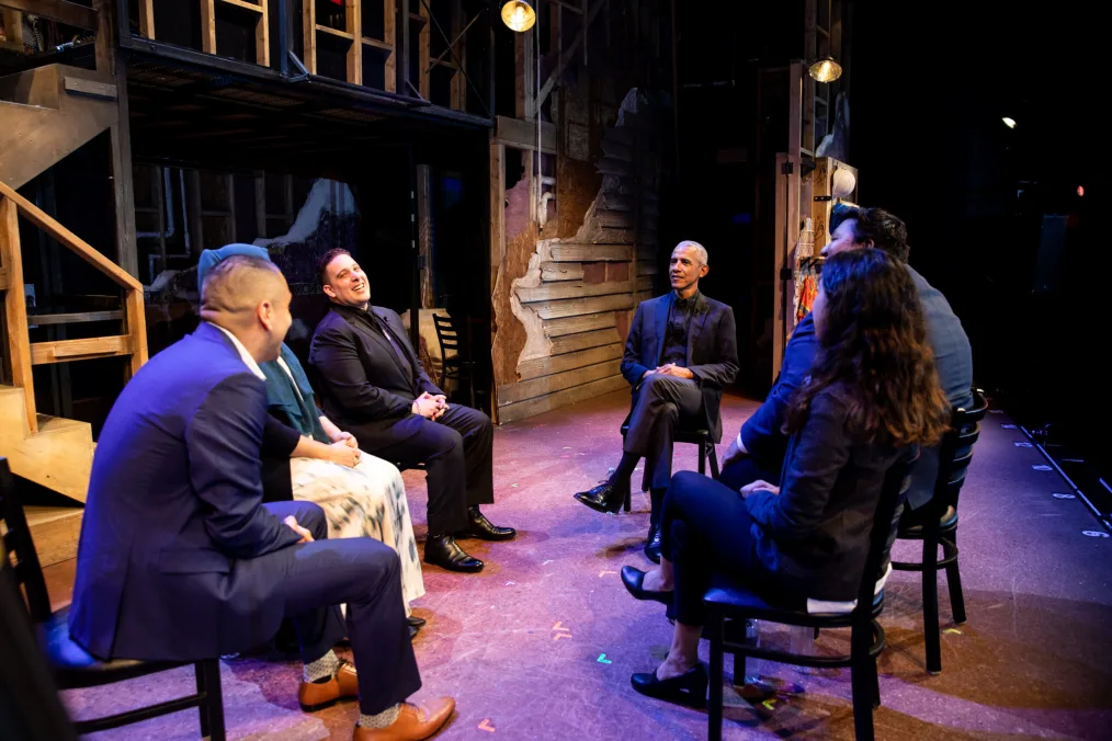 President Obama sitting on stage talking to five other people wearing formal clothing 