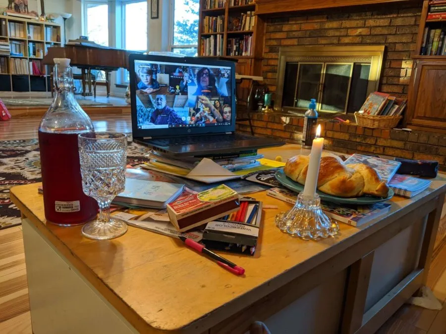 A laptop featuring Deborah's family is set up in front of their Shabbat meal. 