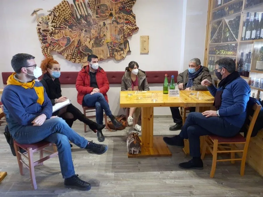 A group of people wearing mask sit around a table in conversation.