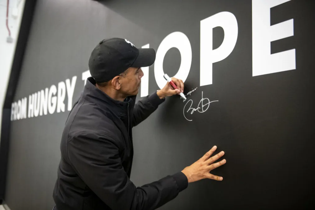 President Obama writes his signature on a black wall that says "FROM HUNGRY TO HOPE."