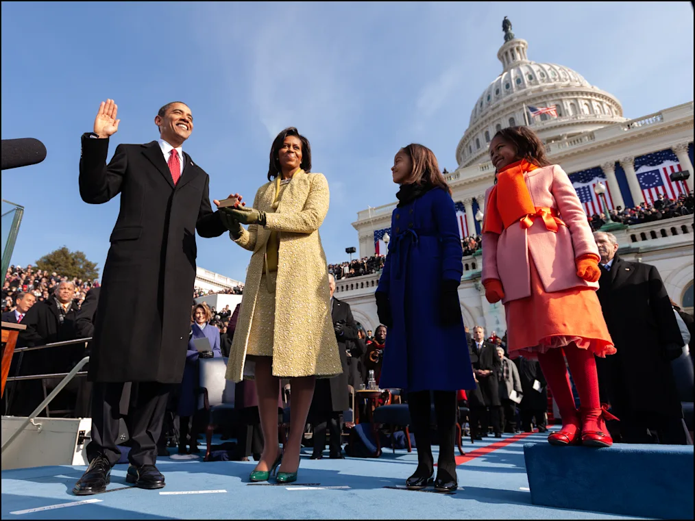 On inauguration Day, President Obama places his left hand on the bible and his right in the air as he sworn in as the President of the United States on January 20, 2009. Mrs. Obama, Malia, and Sasha stand beside him. Mrs. Obama’s hand is also on the bible. 