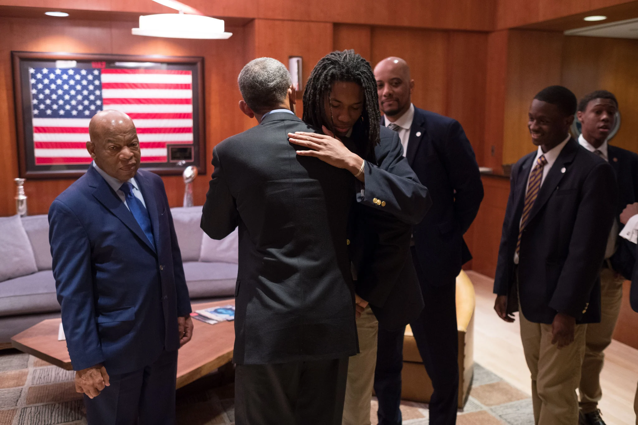 Barack Obama hugging a young man with dreads infront of other men wearing suits, all brown skin
