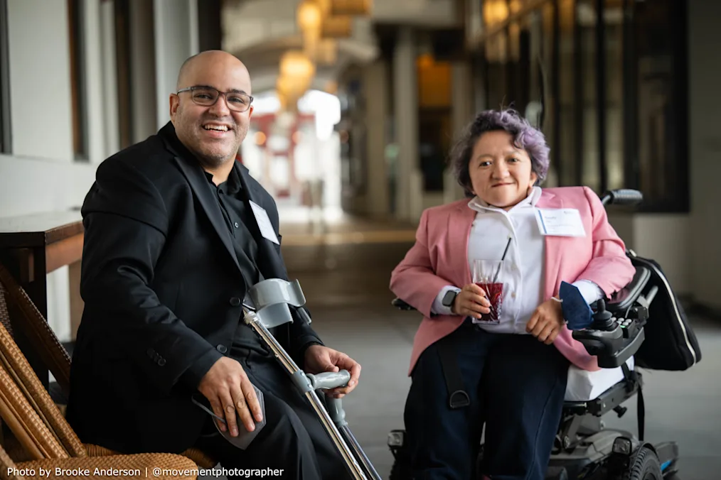 Ryan Easterly, a Black man with a light skin tone, on the right poses for a photo with Sandy Ho, an Asian woman with a light skin tone. Both are dressed professionally and smiling. 