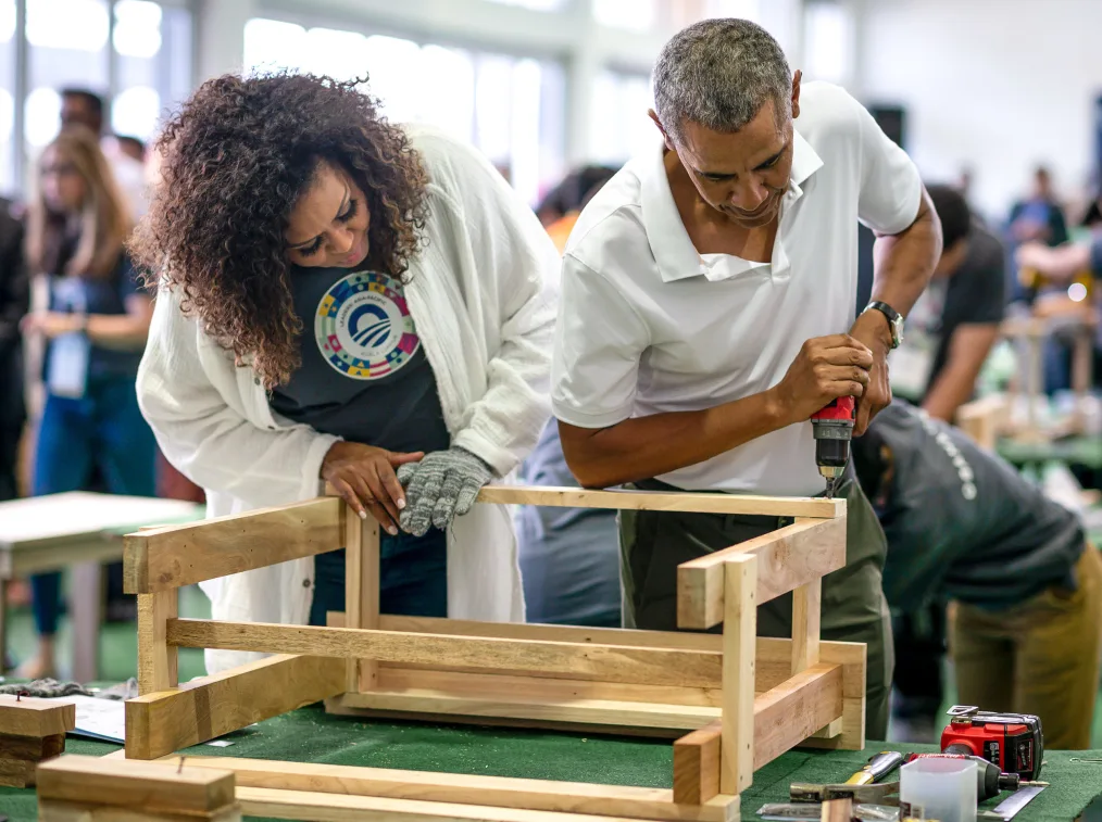 President Obama drills into a piece of furniture as Mrs. Obama looks on.