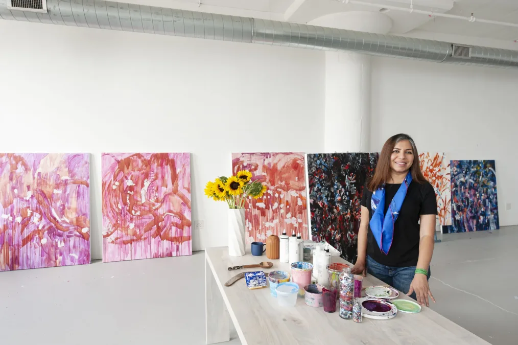 Pooja poses in her studio with her large paintings in the background. 
