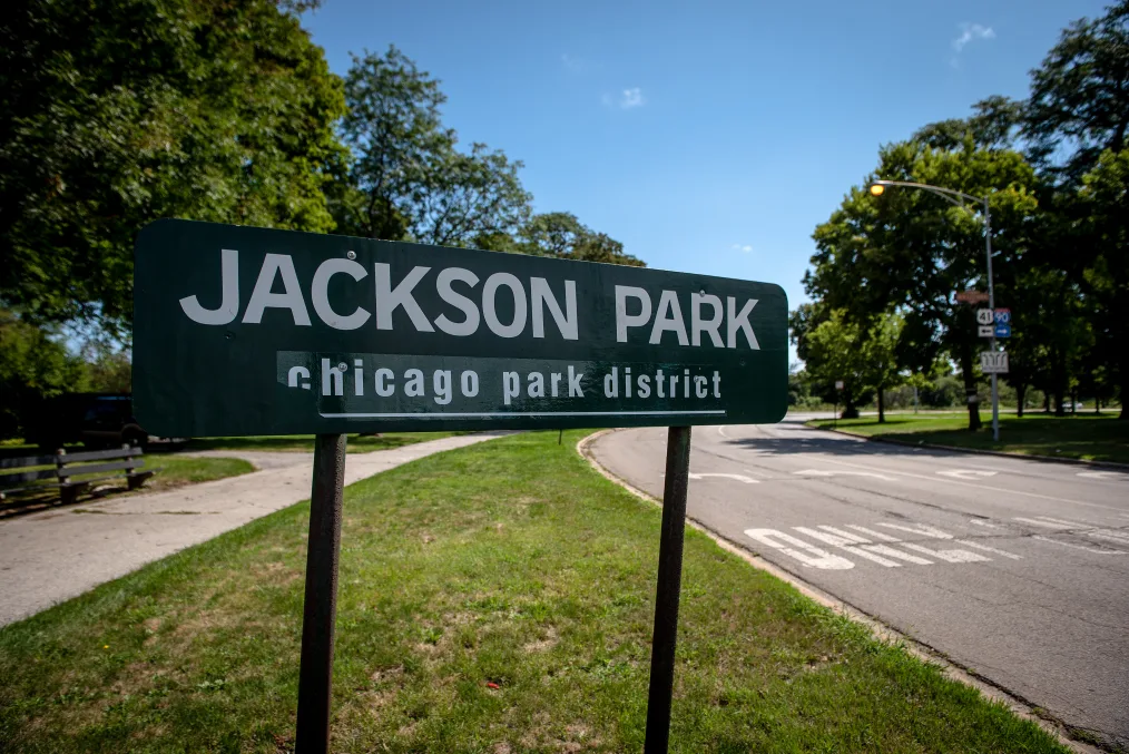 A dark green sign on the side of a curving road that reads, "JACKSON PARK, chicago park district"
