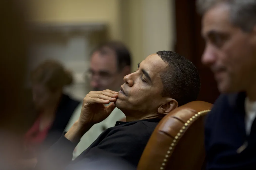 President Obama leans back in his chair with a hand resting on his chin.