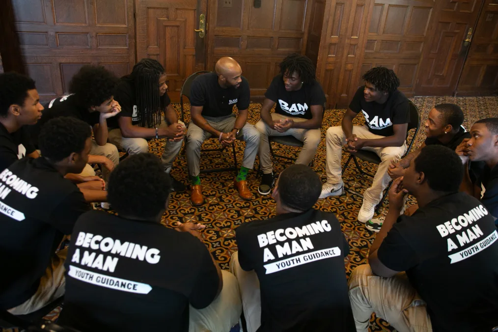 A group of young men sit in a circle in conversation.