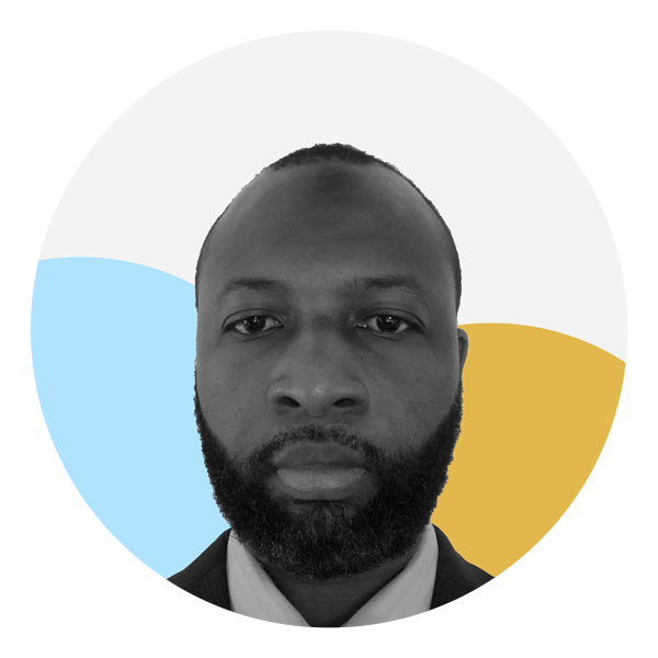 A Black man with buzz cut hair and a full beard and mustache is facing the camera with a straight expression. He is wearing a collared shirt and dark Blazer. The photo is black and white and the background features two circles, one which is light blue and the other yellow. 