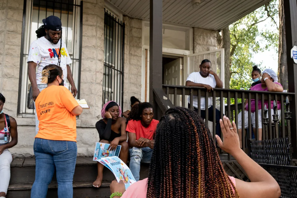 Pastor Tracey gestures to a group of forlorn people standing on the front porch of their home.