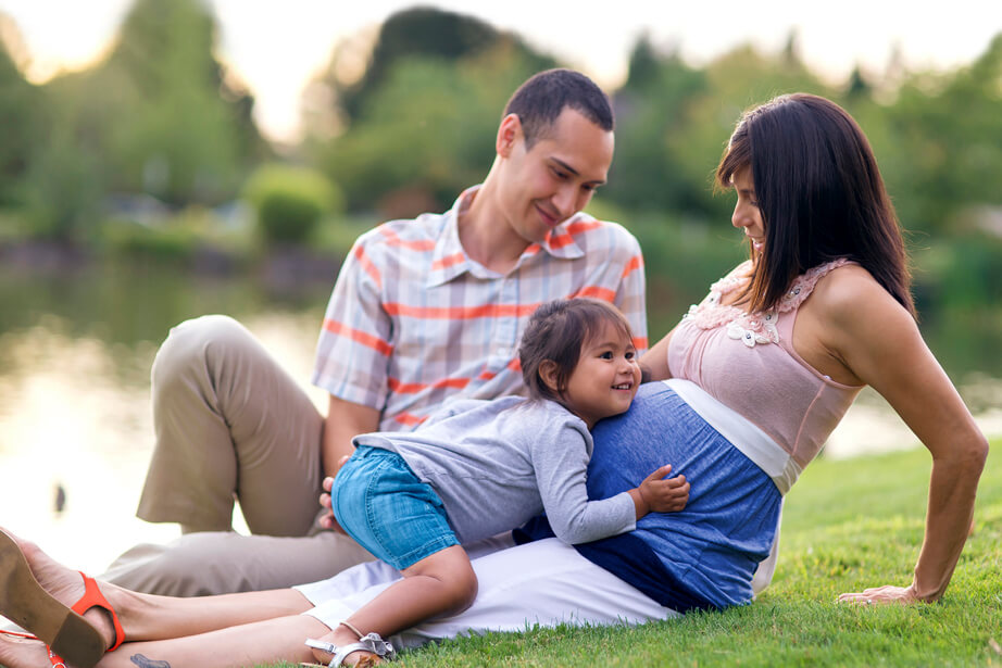 Toddler lying on pregnant mom beside dad on grass