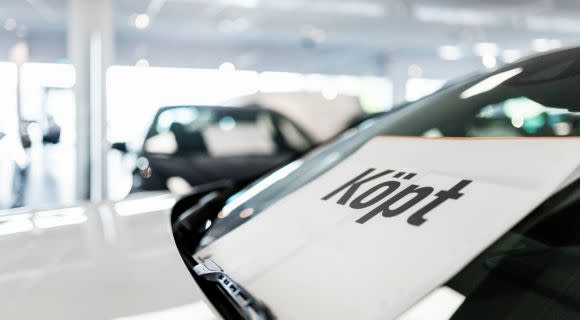 Närbild på en bil med "Köpt" text på vindrutan i en ljus bilhall med andra fordon i bakgrunden.