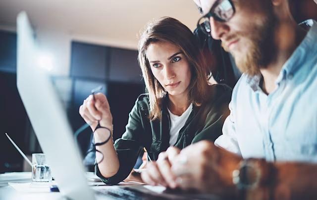 Två kollegor arbetar tillsammans vid en bärbar dator på ett kontor, koncentrerade på skärmen.