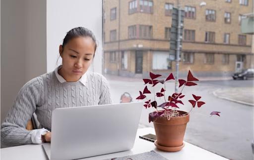Kvinna sitter framför fönster och jobbar på sin dator. 