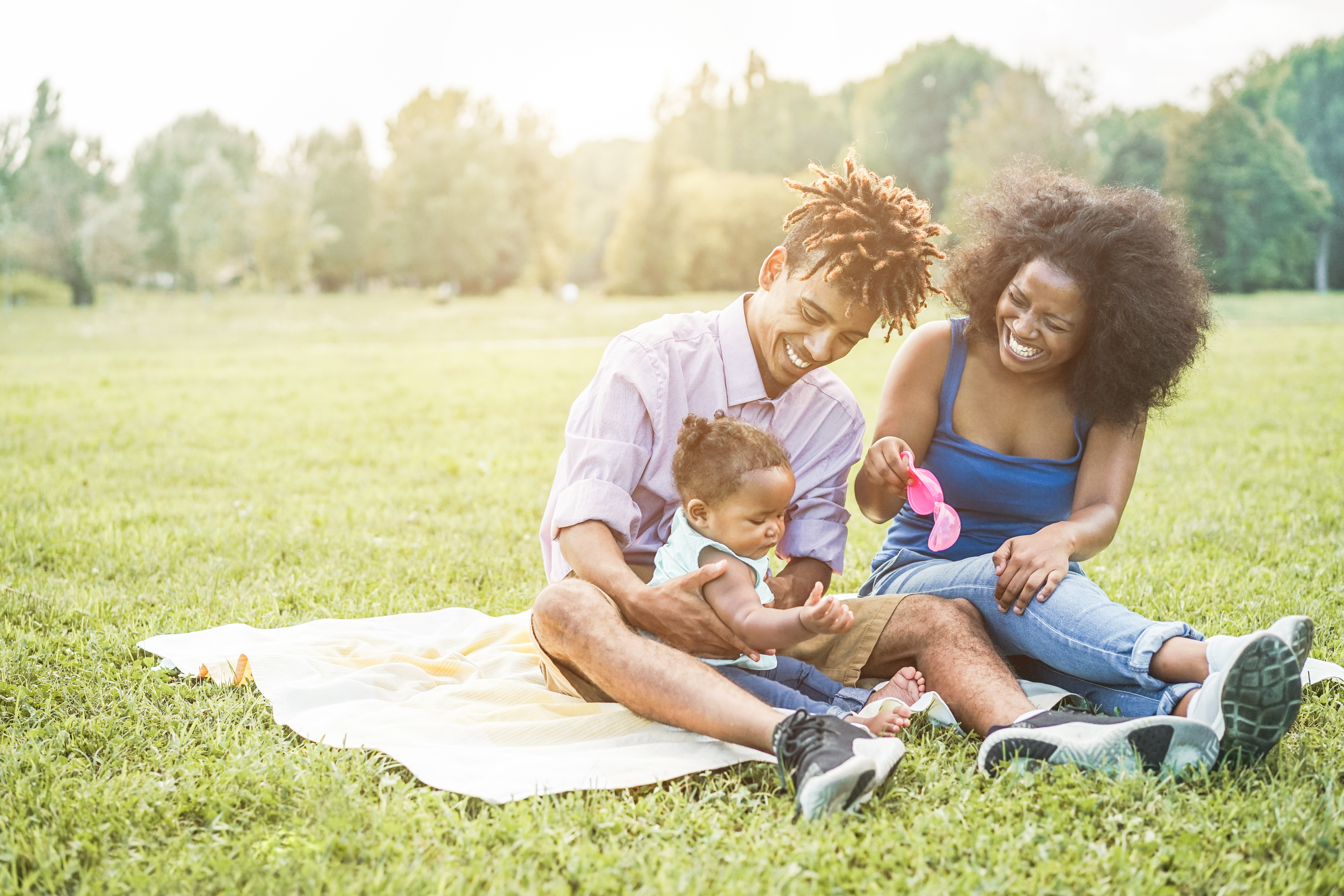 A woman sitting on the grass and a man with a little girl on his lap sitting on a blanket.