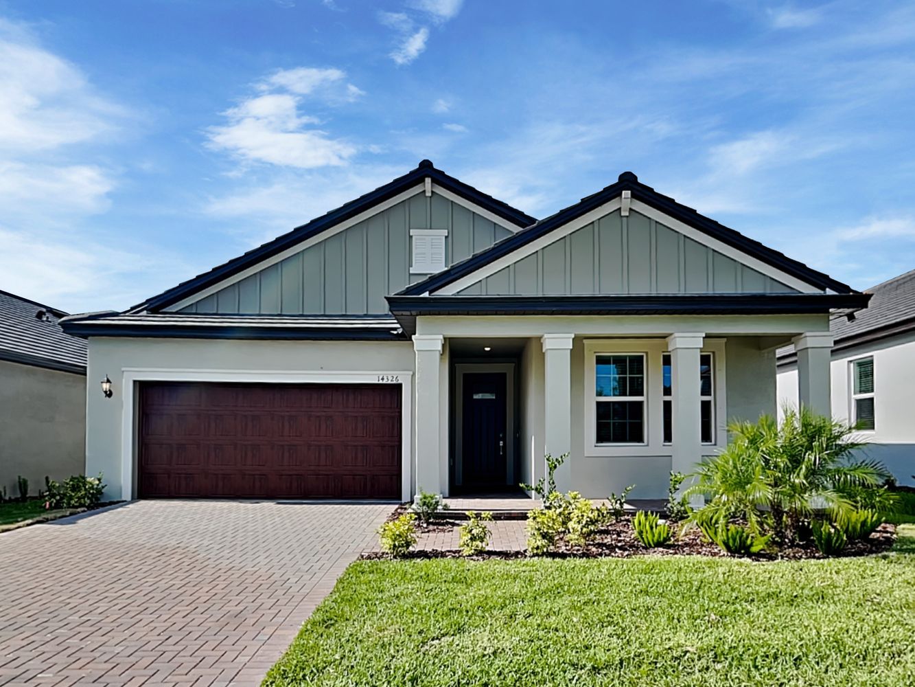 florida front of home image with a brown garage tan exterior and red brick driveway