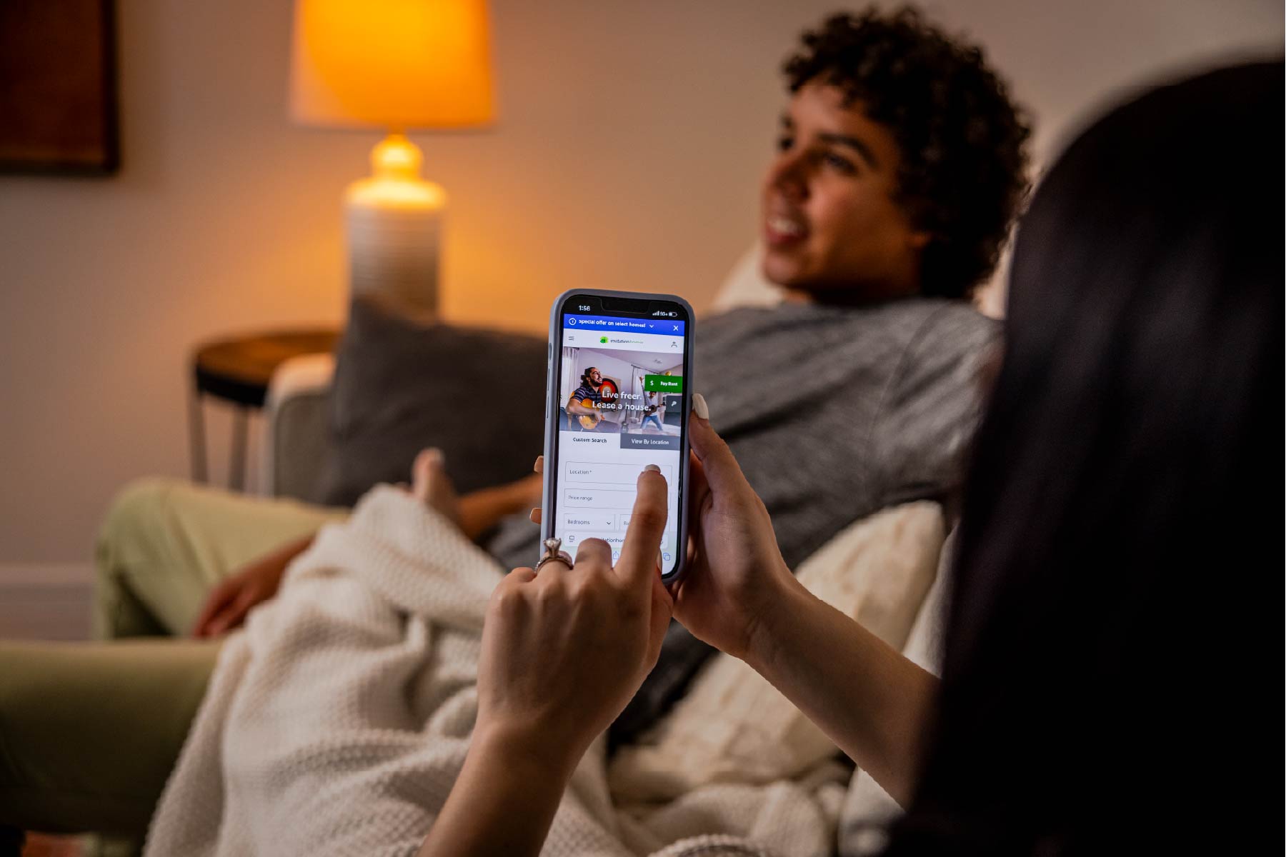 A woman requests service from Invitation Homes from the Invitation Homes app while sitting on the couch. 