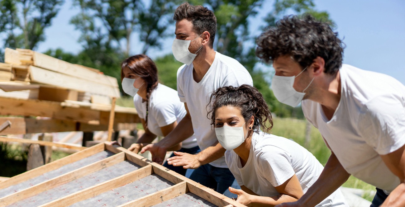 A group of people wearing face masks helping to build a house