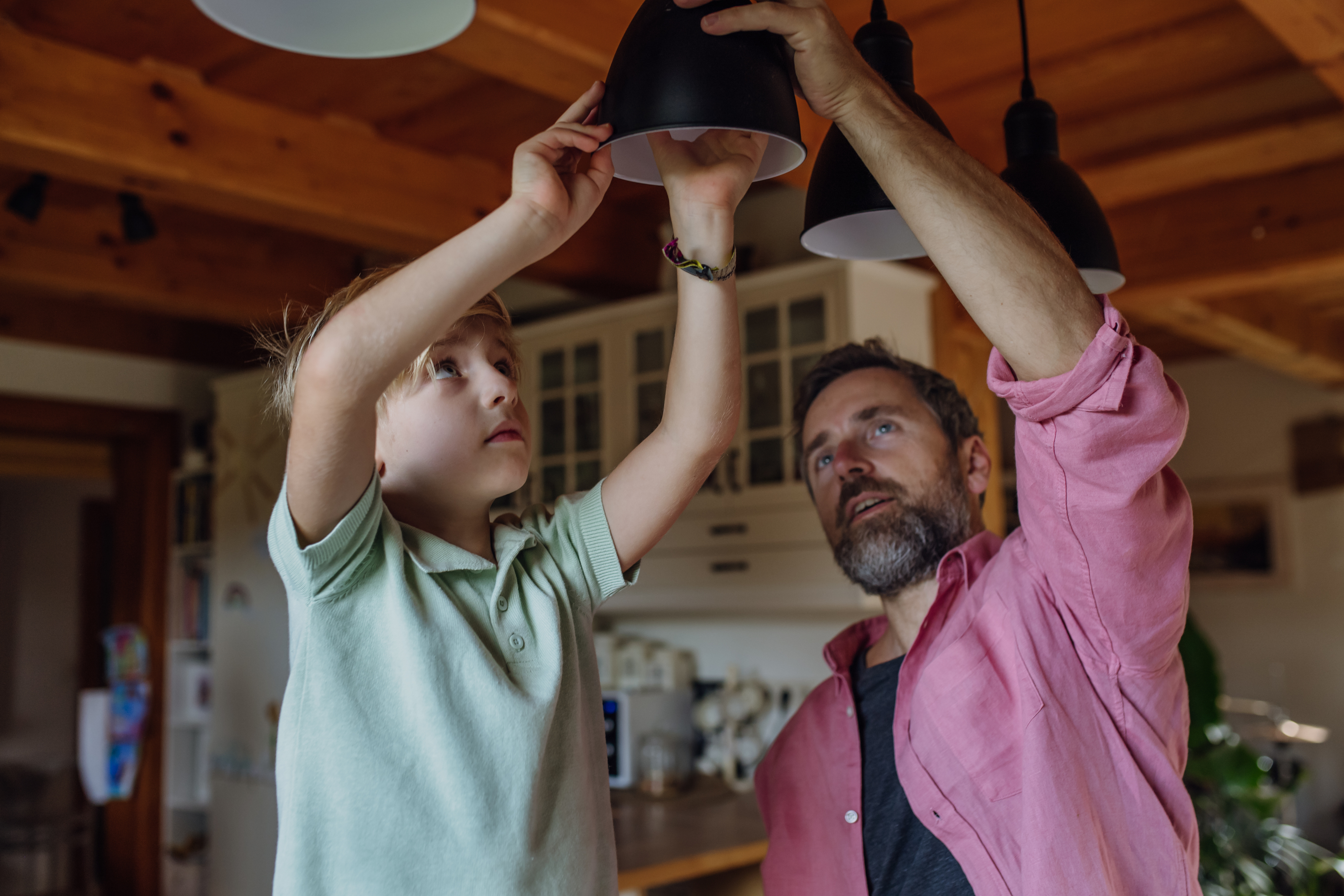 A dad and his son screwing in a lightbulb into a overhead lamp shade.