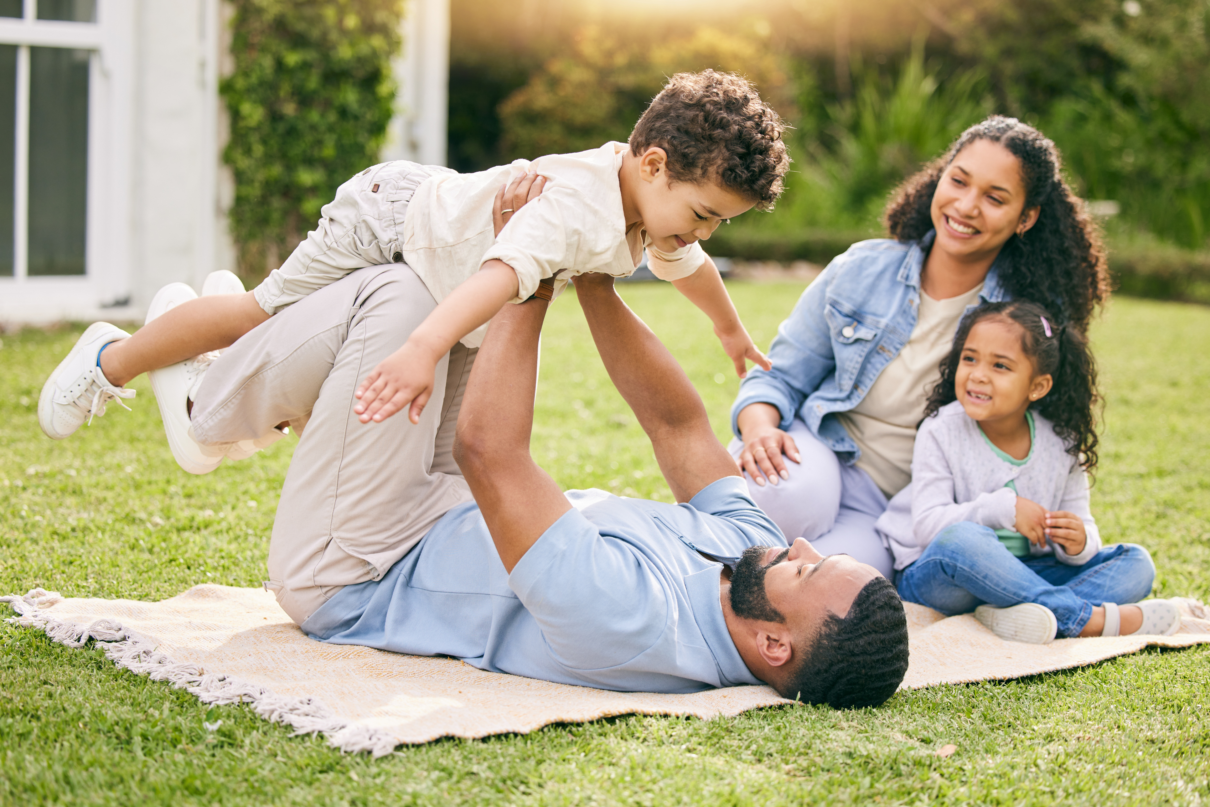 A young family on a picnic blanket with the dad holding his son above him. 