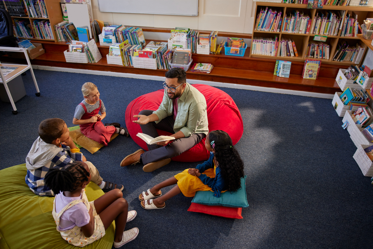 A man in four kids sit on the floor of a library