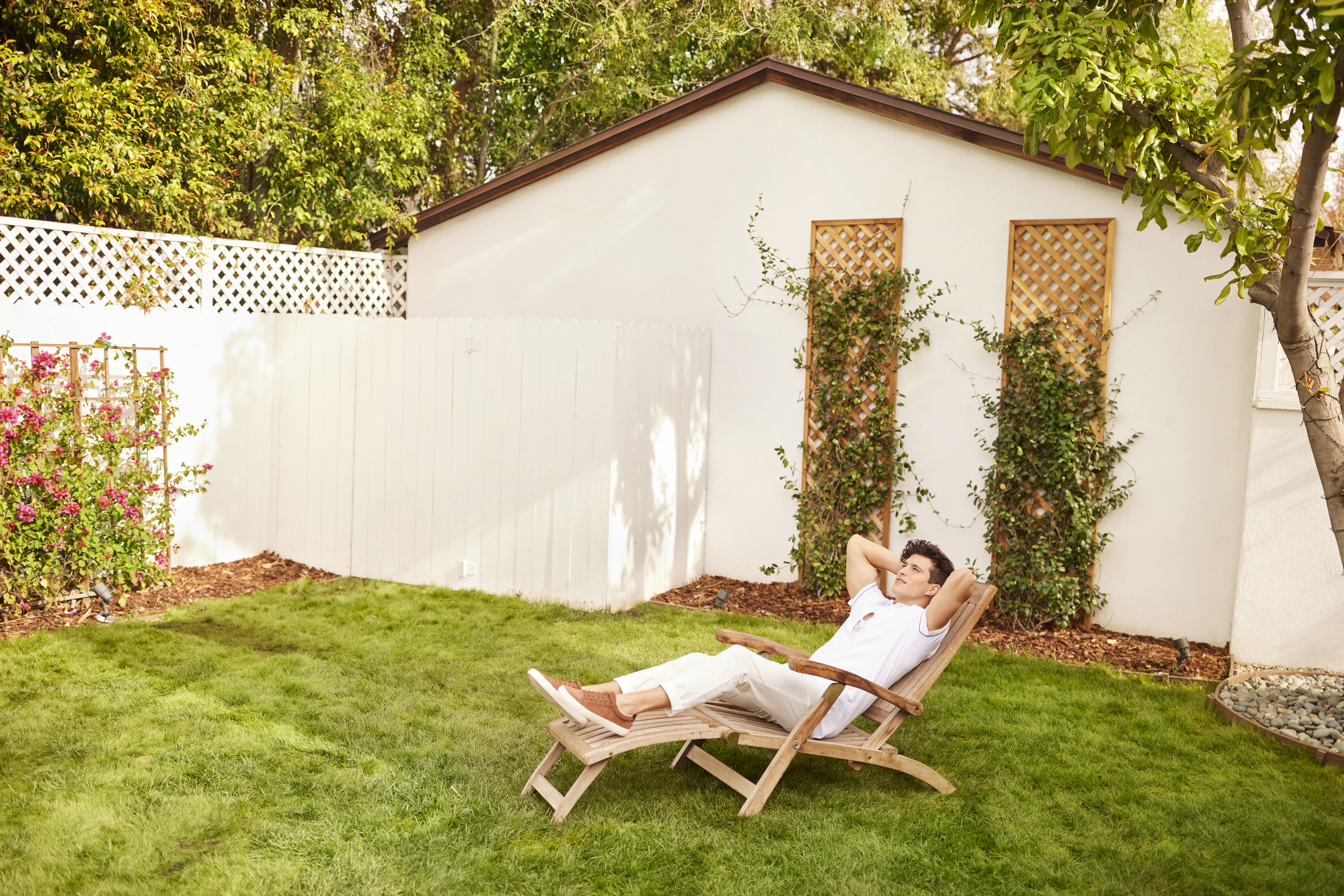 Young man sitting in his fenced backyard. 