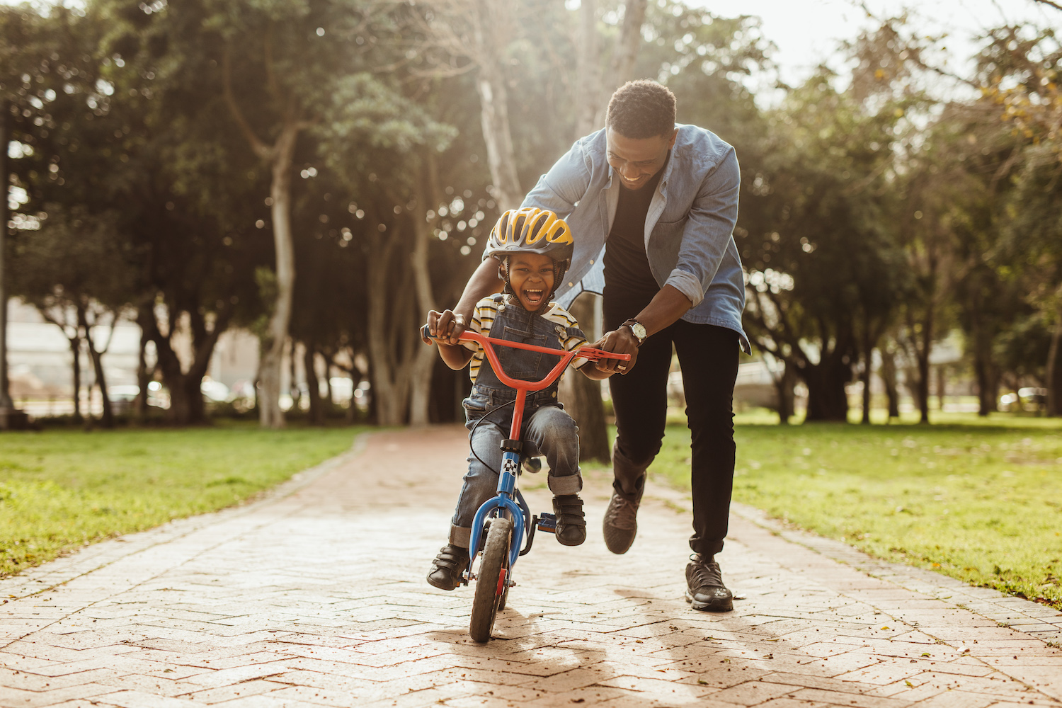 Dad helping his son learn how to ride a bike on a path through a park