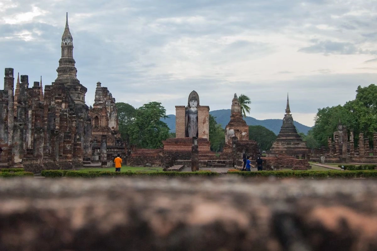 Ancient ruins of Wat Mahathat temple in Sukhothai Historical Park, Thailand, with clear blue skies and surrounding greenery