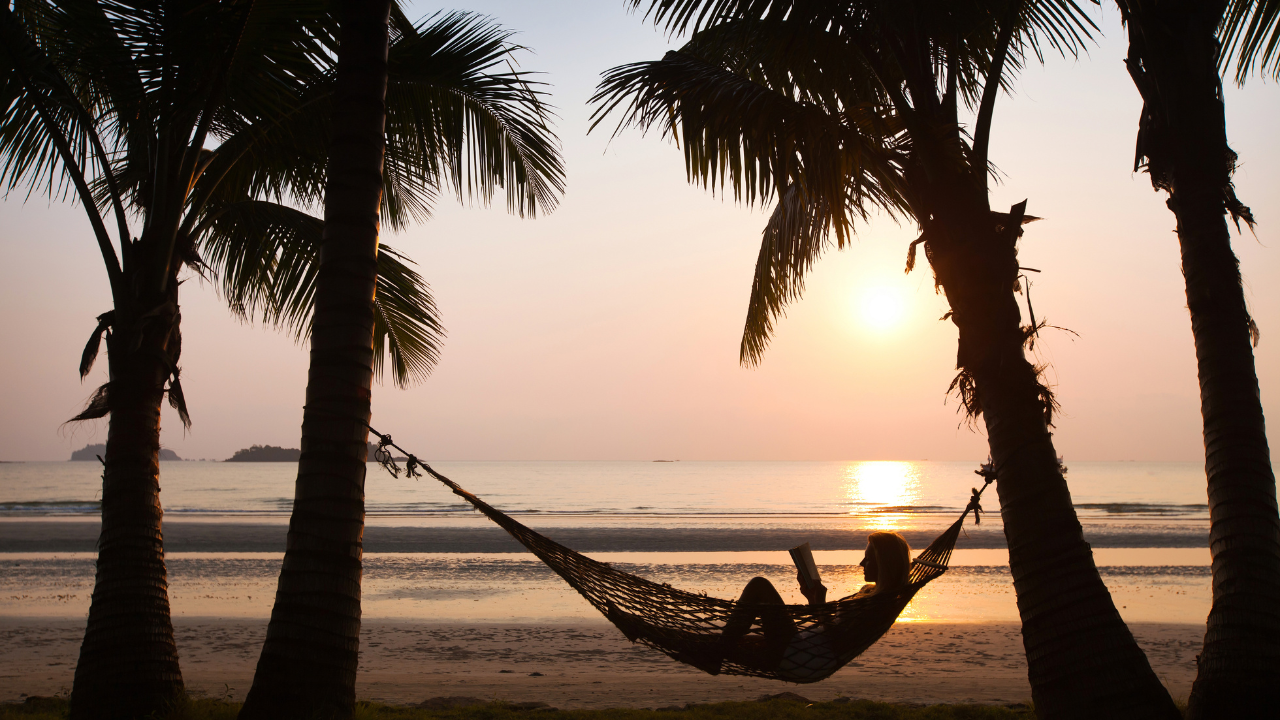 https:A calming beach scene with a suitcase and palm tree silhouette. Overlaid on the image are astrological symbols representing Mercury in retrograde and crescent moons, signifying a smooth vacation despite cosmic influence.