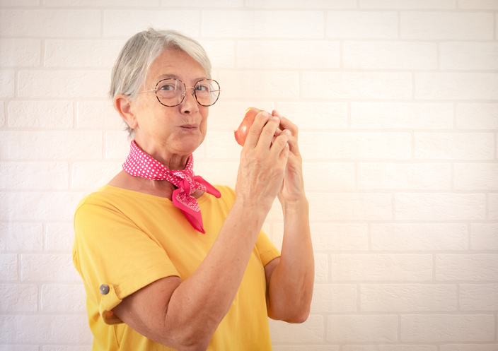 An older lady wearing a yellow t-shirt stands against a plain white backdrop.