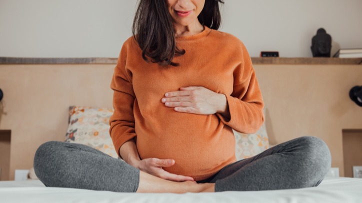 Cropped Pregnant woman, sitting in crossed legs in be at home holding her belly