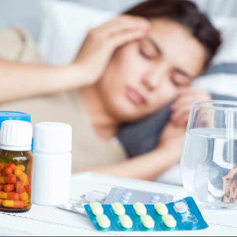 Woman Resting in Bed with Migraine Medication on the Table