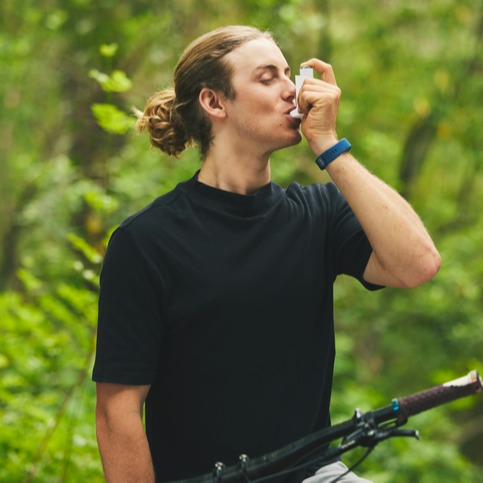 Asthma, fitness and man cyclist on a bicycle in a forest with breathing medical emergency during exercise or training. Outdoor, lung support and athlete with inhaler in nature for workout or wellness 