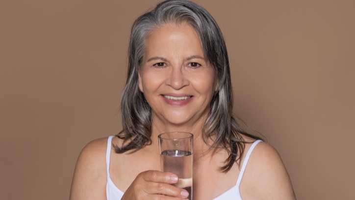 Happy older gray-haired European woman drink a glass of water, enjoy morning routine