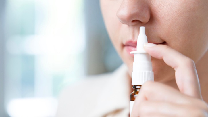 Close-up shot of sick young woman using nasal spray