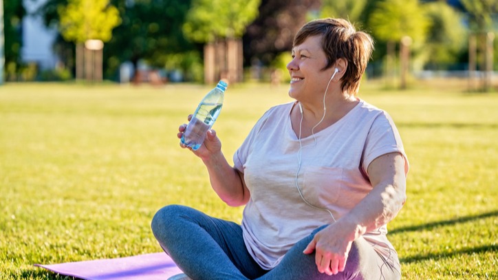 Relaxed senior plus size woman with earphones sitting on yoga mata