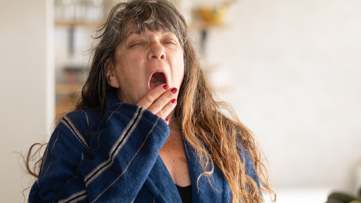  A mature woman is yawning and looking sleepy because of an allergy medicine she is taking that makes her drowsy.