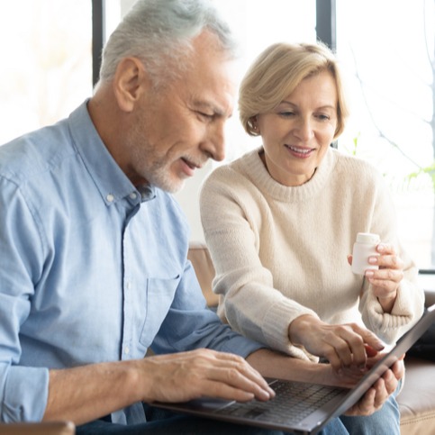 Senior couple with pills and laptop in living room