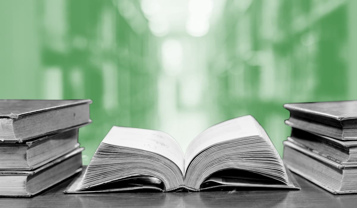 Stack of books on a desk with one open book in the center.