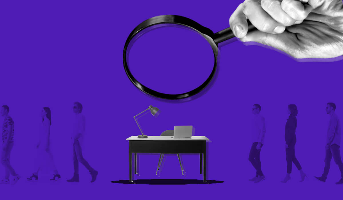 A magnifying glass focused on an empty desk surrounded by employees walking by, resembling talent gaps organizations can close with people analytics.