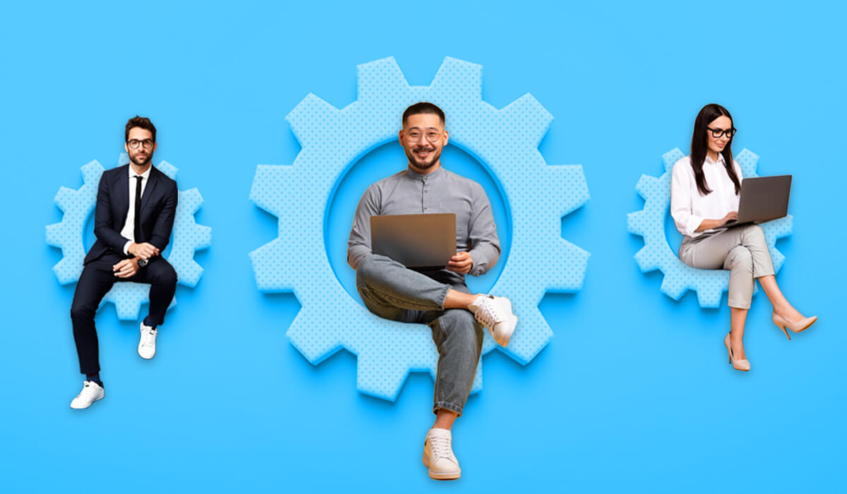 Three people are seated on a giant gear wheel, focused on their laptops, symbolizing workforce optimization.