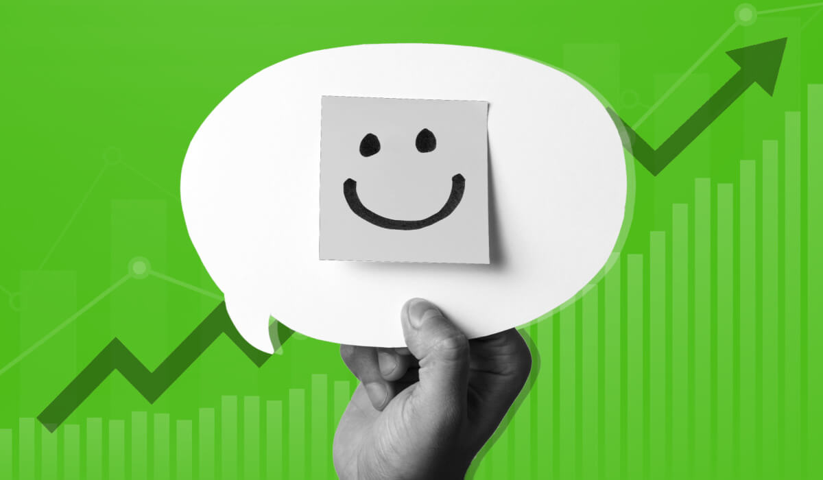 Hand holding a speech bubble with a post it note with a happy face on it, overlayed on top of a graph trending up and to the right to signify employee engagement strategies