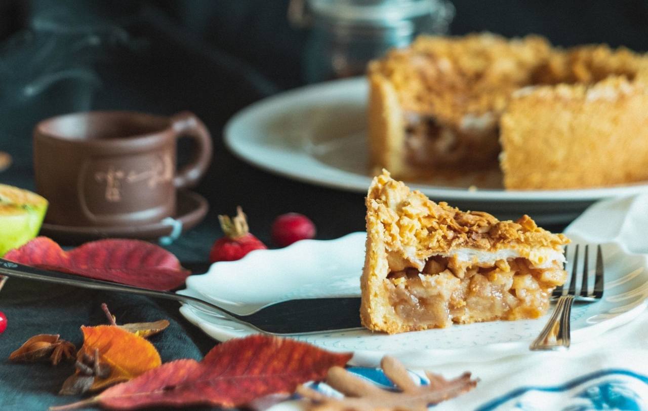 A piece of apple pie with a fork on a table covered in leaves.