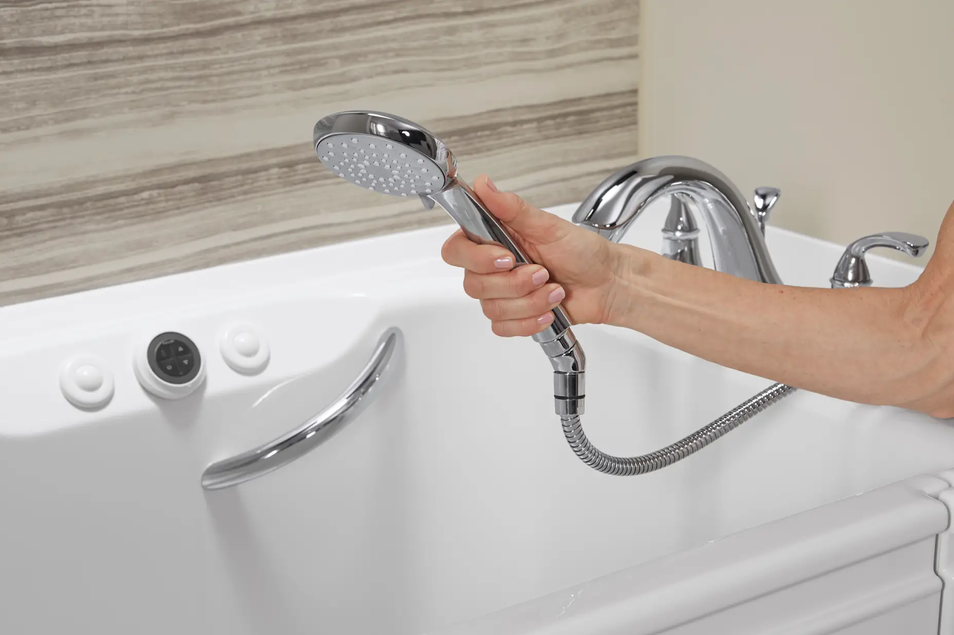 A close up shot of a hand holding a detachable showerhead on a walk-in tub.