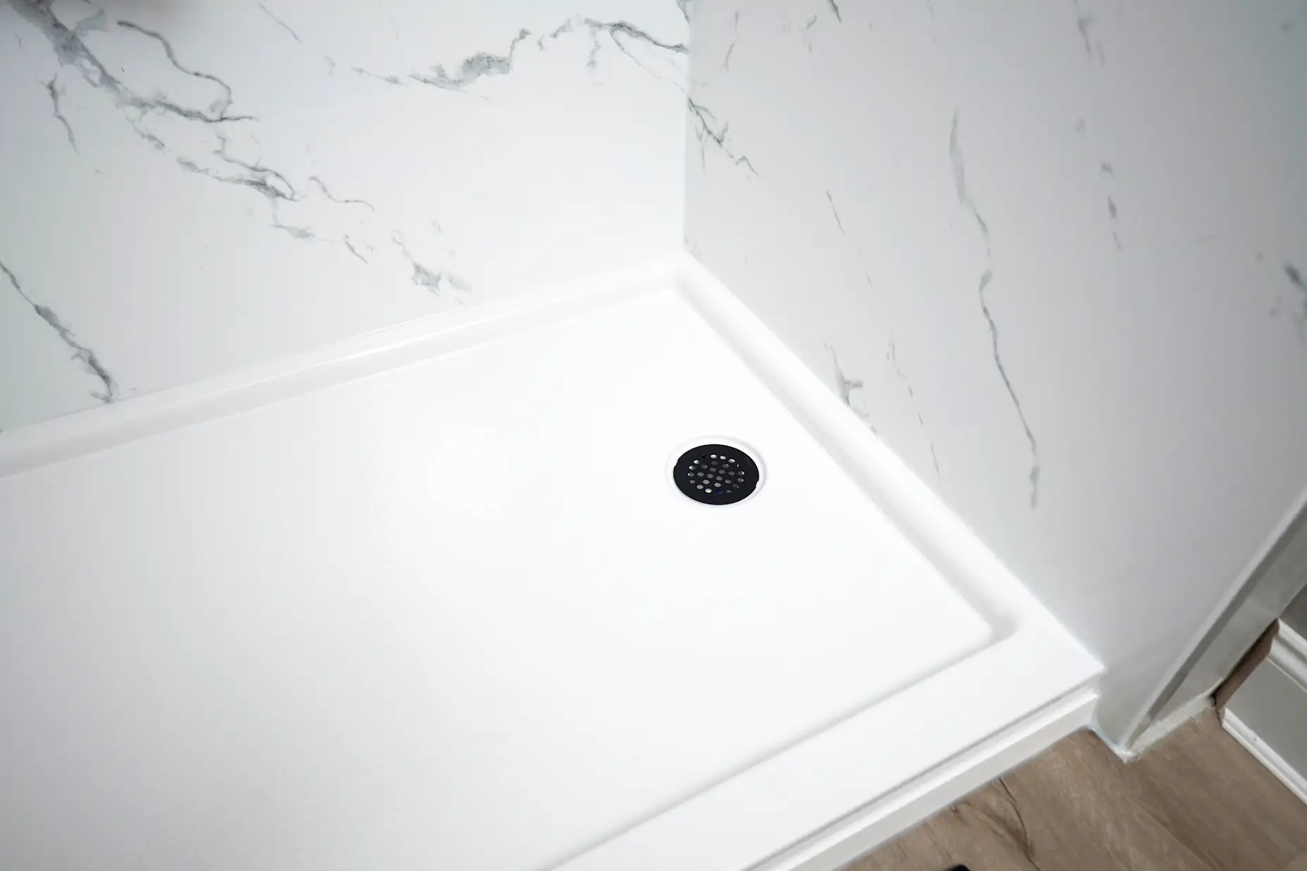 A close up image of a white acrylic shower pan with a circular drain. 