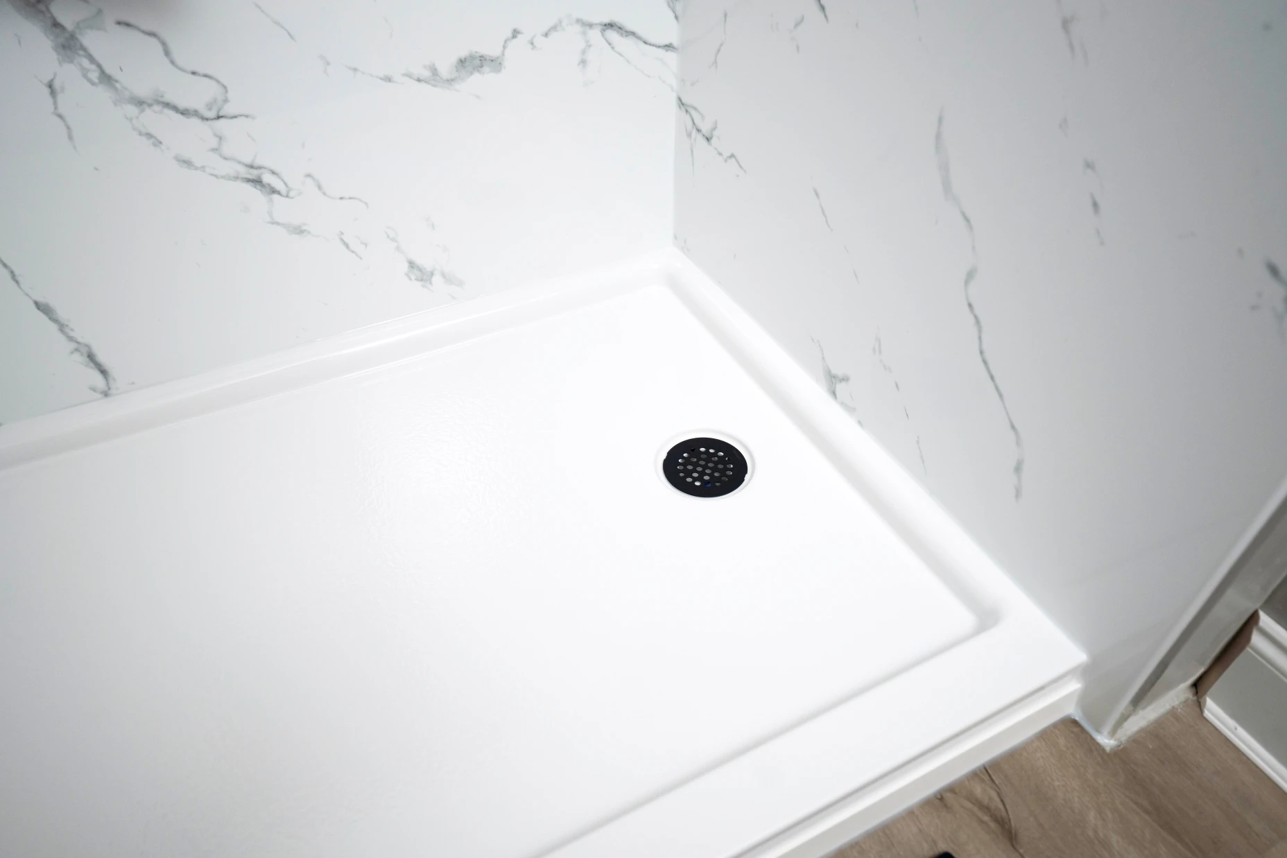 A close up image of a white acrylic shower pan with a circular drain. 