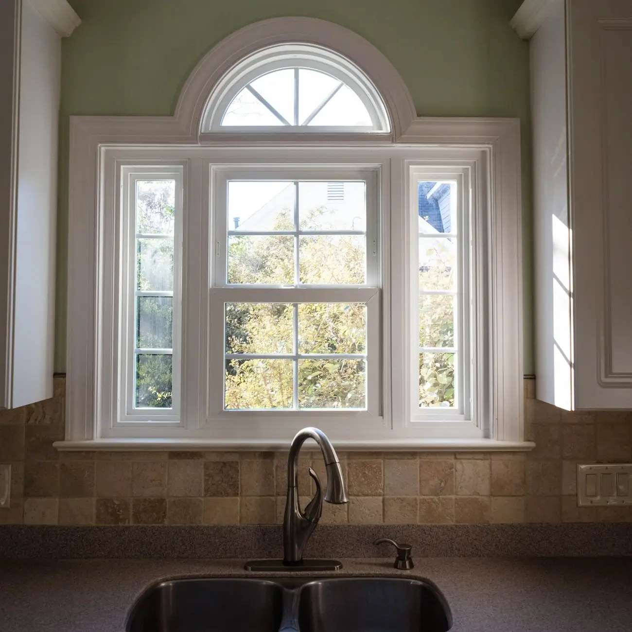 A speciality double hung window over a kitchen sink overlooking a backyard.