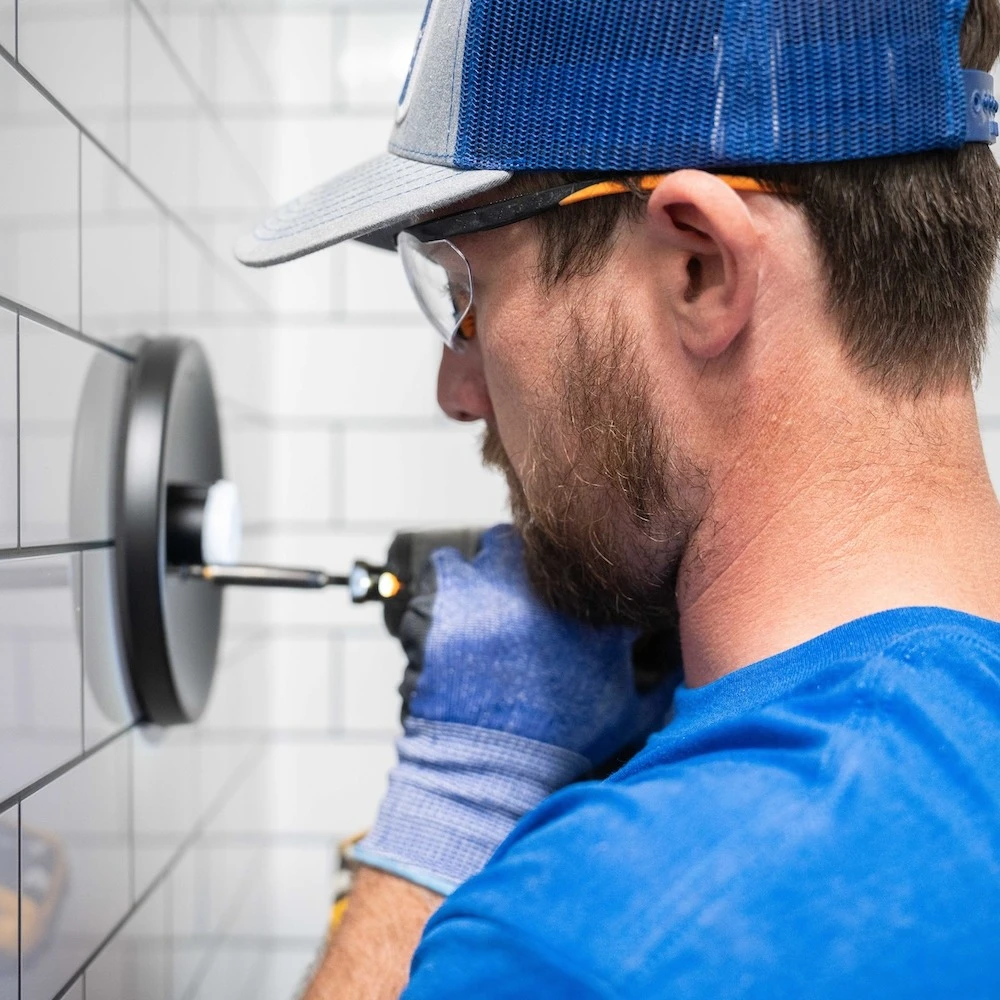 A man installing a shower head into a shower wall. 