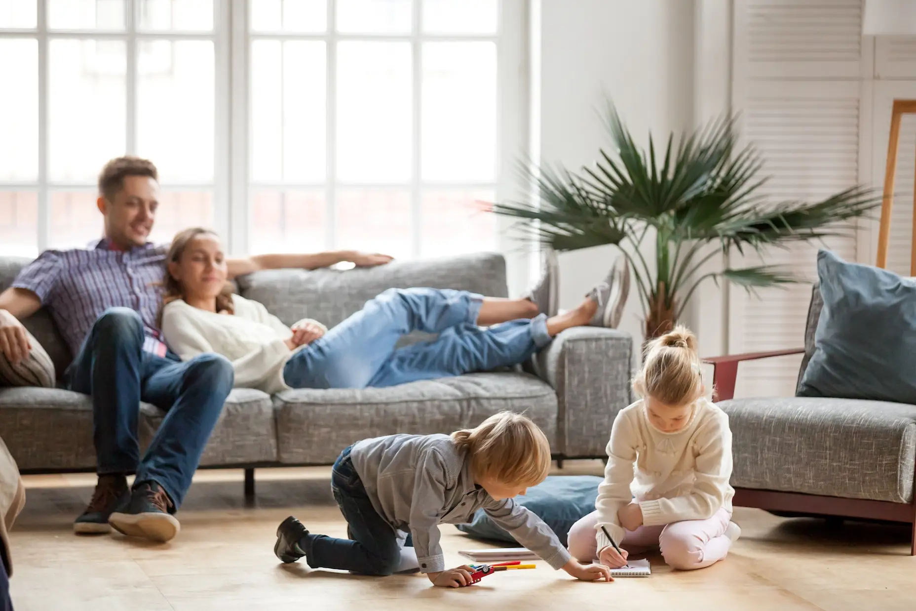 A family relaxing in the living room in front of a large window.